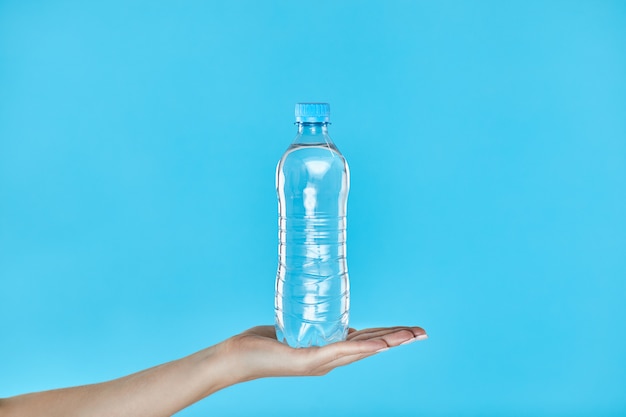 Kobieta wręcza trzymać butelkę woda na błękicie.