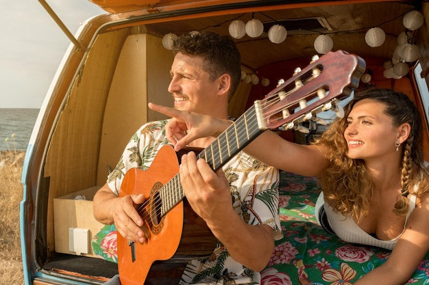 Kobieta wskazująca na horyzont, podczas gdy mężczyzna gra na gitarze siedząc w furgonetce