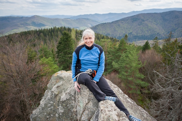 Kobieta wspinacz na szczycie skały ze sprzętem wspinaczkowym