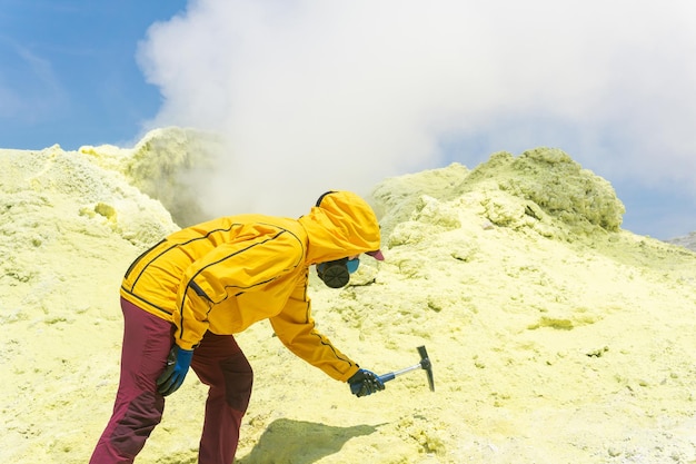 Kobieta wulkanolog na zboczu wulkanu obok dymiącego fumarolu pobiera próbkę minerału z krawędzi krateru siarki