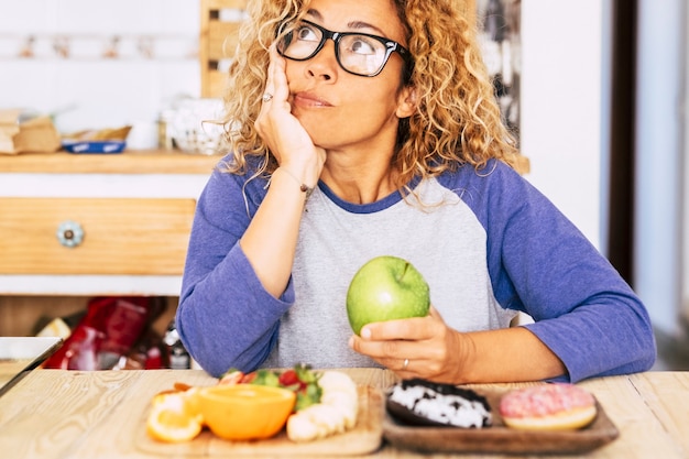 Zdjęcie kobieta wybiera jabłko lub pączek - dieta i dobre odżywianie styl życia, owoce i pączki na stole - w domu w domu