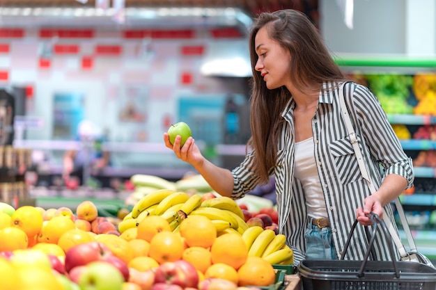 Kobieta wybiera świeże zielone jabłko w dziale owoców supermarketu. Klient kupujący jedzenie w sklepie spożywczym