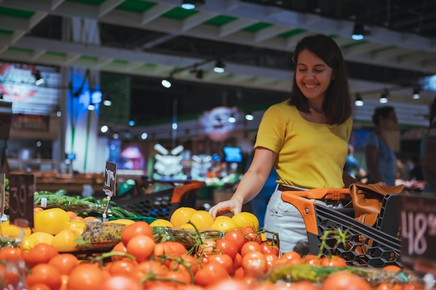 Kobieta wybiera żółte pomidory z półki sklepowej zakupy spożywcze