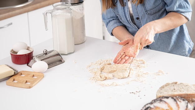 Kobieta wycina foremkę do ciastek z ciasta na tle biały stół kuchenny.