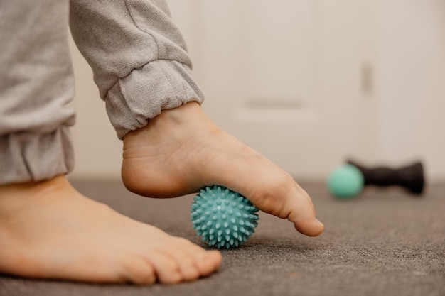 Kobieta wykonuje ćwiczenia gimnastyczne korekcyjne płaskostopia przy użyciu piłki do masażu Mięśniowo-powięziowe rozluźnienie mięśni stóp Paluch koślawy Ból Identyfikacja płaskostopia Praktyki samoopieki w domu Opieka zdrowotna