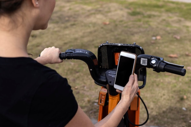 Kobieta z Ameryki Łacińskiej korzystająca z aplikacji do wypożyczania rowerów na telefonie komórkowym