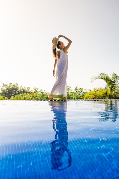 Kobieta z białą suknią obok odkrytego tropikalnego basenu