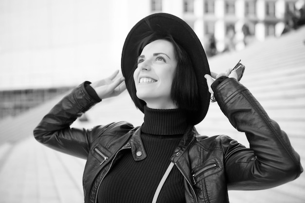 Kobieta z brunetką uśmiechem w czarnym kapeluszu, kurtce, ubraniach na schodach. Koncepcja akcesoriów mody. paryżanka