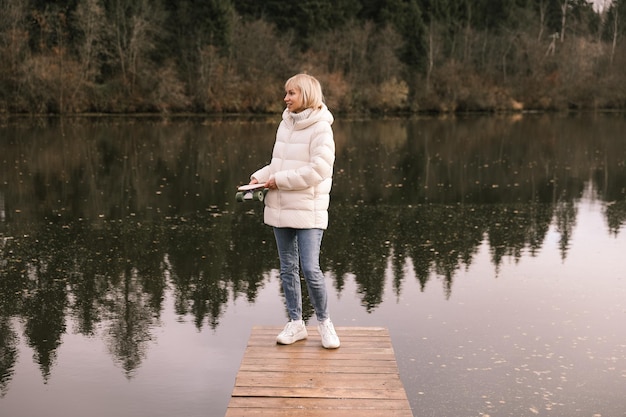 Kobieta z deskorolką spaceruje po jesiennym parku nad rzeką, uczy się jeździć na łyżwach, spędza weekend na świeżym powietrzu na świeżym powietrzu. Koncepcja zdrowego sportu.