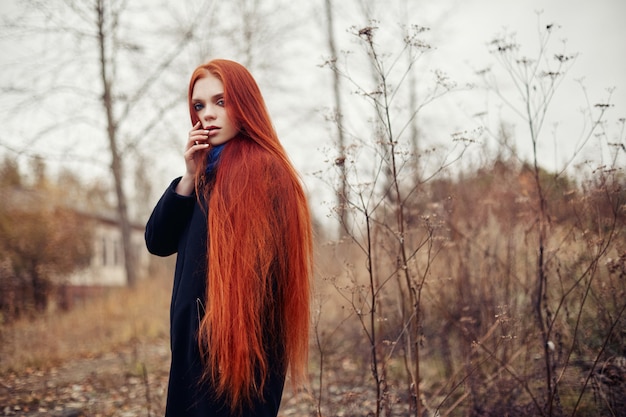 Kobieta z długimi rudymi włosami spacery jesienią na ulicy. Tajemniczy marzycielski wygląd i wizerunek dziewczyny. Rudzielec kobieta chodzi w jesieni miasto. Zimna pochmurna jesień w mieście