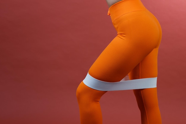 Kobieta z ekspanderem na nogi w pomarańczowym stroju sportowym fitness studio na białym tle strzał z bliska