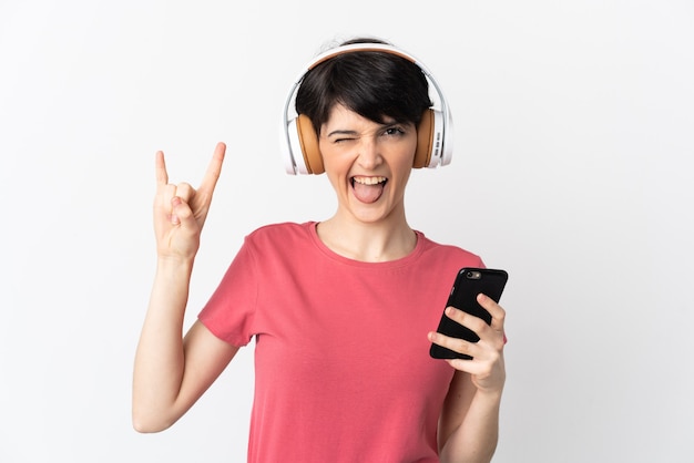 Kobieta Z Krótkimi Włosami Na Białym Tle Słuchanie Muzyki Z Telefonu Komórkowego Robi Rockowy Gest