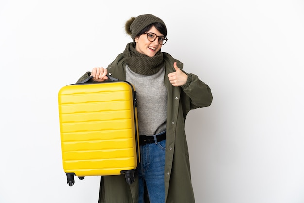 Kobieta z krótkimi włosami na białym tle w wakacje z walizką podróżną iz kciukiem do góry