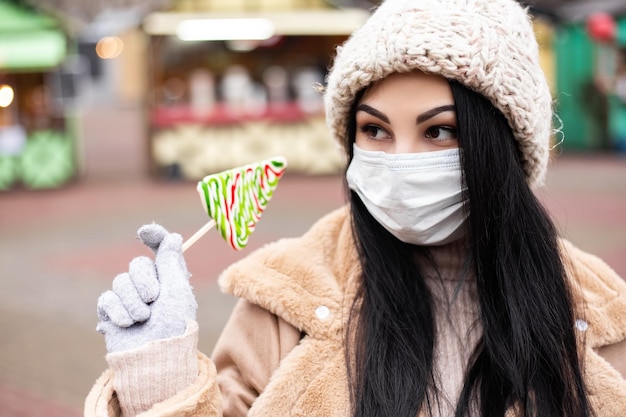 Zdjęcie kobieta z maską na twarz trzyma cukierki, stojąc na zimowych targach wakacyjnych