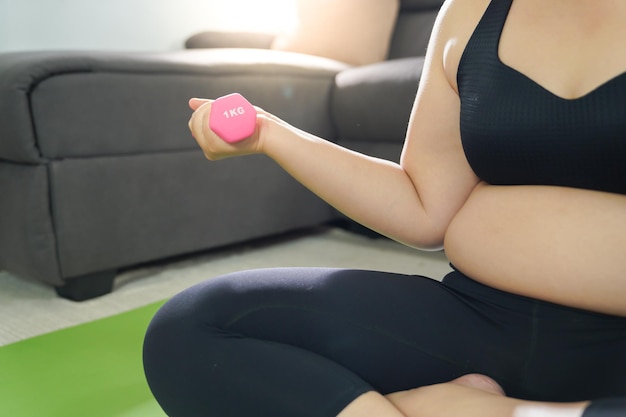 Kobieta z nadwagą ćwicząca do ćwiczeń odchudzających z hantlami w pozycjach rozciągających w domu w salonie Wesoła gruba kobieta dieta koncepcja zdrowego stylu życia