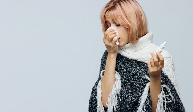 Zdjęcie kobieta z papierową serwetką kichanie, używając sprayu do nosa, aby sobie pomóc. alergia, grypa