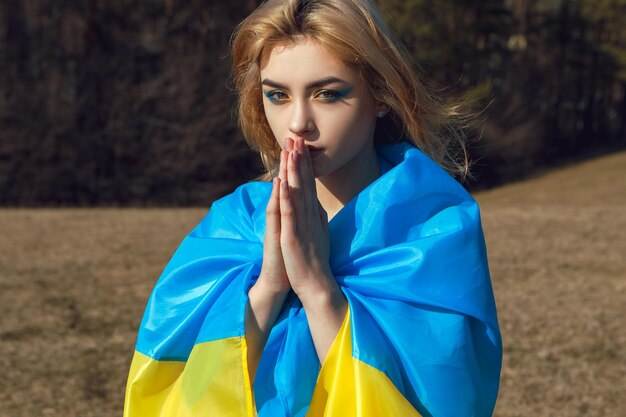 Kobieta z patriotycznym makijażem owinięta ukraińską flagą i modląca się Stoisko z koncepcją Ukrainy