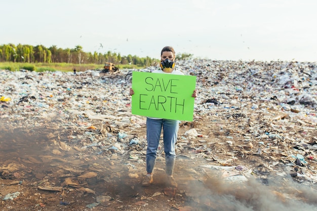 Zdjęcie kobieta z plakatem ratuje planetę, pikietuje skażone śmieciami środowisko, płonący ogień i czarny dym