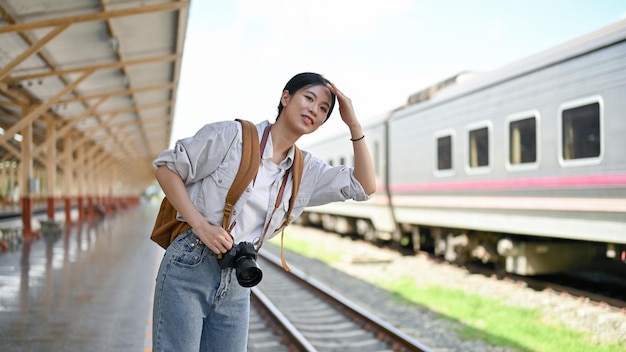 Kobieta z plecakiem stoi na peronie i czeka na swój pociąg w słoneczny dzień