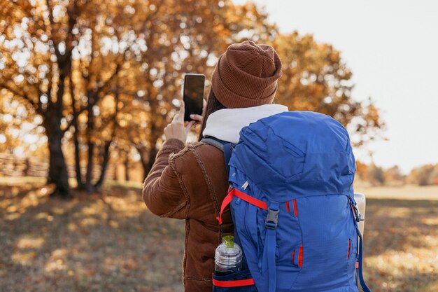 Kobieta z plecakiem ze smartfonem robiąca zdjęcia w jesiennym lesie podczas podróży