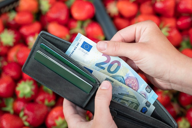 Zdjęcie kobieta z portfelem i pieniędzmi w dłoniach płacąca za truskawki świeżo zebrane jagody na rynku banknoty euro ekologiczne ogrodnictwo i zdrowe odżywianie