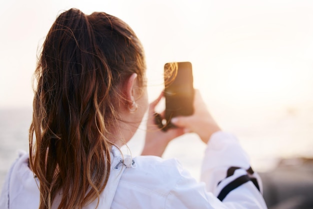 Kobieta z powrotem lub zdjęcie telefonu przedstawiające zachód słońca na plaży nad oceanem lub morzem w środowisku naturalnym wakacje lub miejsce podróży do Kanady Student-turysta lub wpływowy w technologii fotografii mobilnej lub vlog