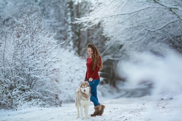 Kobieta z rasowym psem husky na zaśnieżonej leśnej drodze