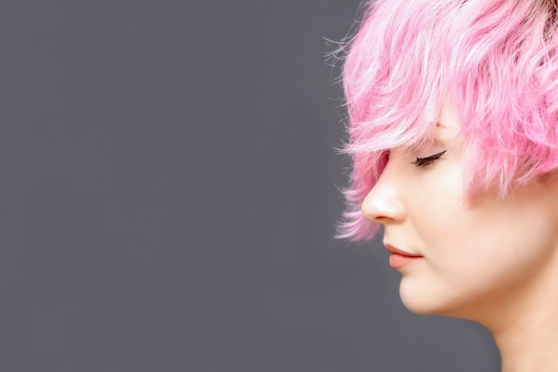 Kobieta z różową fryzurą stoi z zamkniętymi oczami z boku