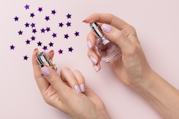 Kobieta z różowym manicure trzyma butelkę perfum na pastelowym tle