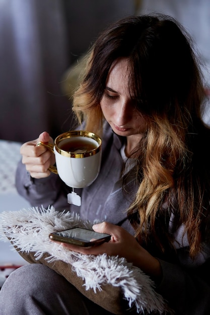 Kobieta z telefonem i filiżanką herbaty przytulny jesienny dom Kurs online nauka języka w aplikacji freelance Relaks i wypoczynek