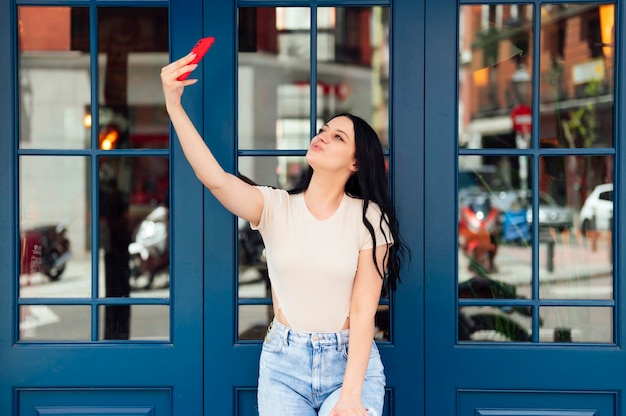 Kobieta z telefonem komórkowym robi selfie, opierając się o ścianę