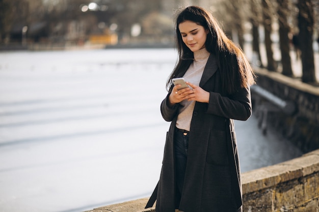 Kobieta z telefonem w parku jeziorem w zimie