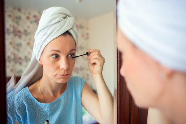 kobieta z umytą głową w ręczniku robi rano makijaż w swojej sypialni.