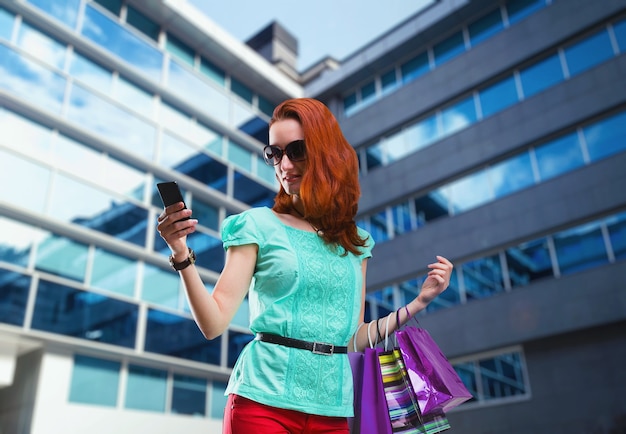 Zdjęcie kobieta z wieloma torbami na zakupy korzystająca z telefonu w pobliżu nowoczesnego centrum handlowego