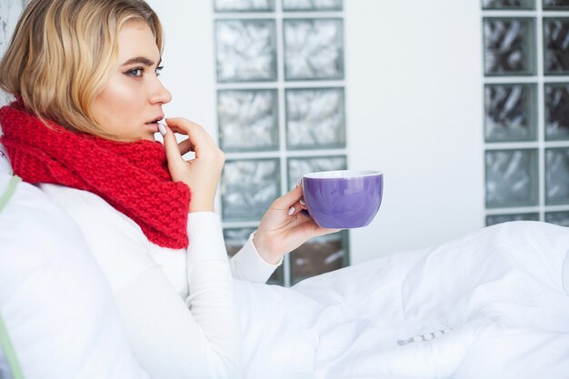 Kobieta z wirusem grypy leżącym w łóżku, mierzy temperaturę za pomocą termometru