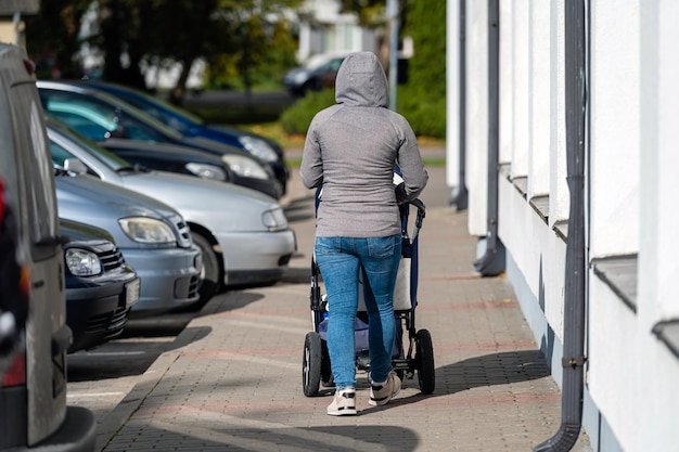 Kobieta z wózkiem dziecięcym idzie chodnikiem wzdłuż ulicy z tyłu