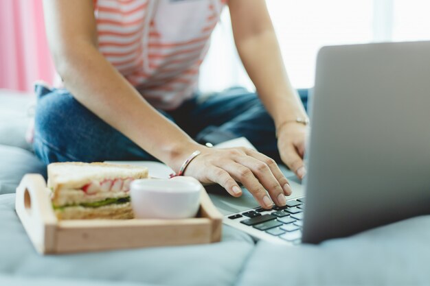 Kobieta za pomocą komputera i śniadanie w łóżku w celu poddania się kwarantannie, dystansu społecznego, pobytu i pracy w domu