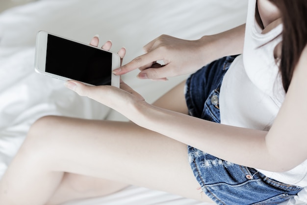 Zdjęcie kobieta za pomocą telefonu komórkowego, siedząc na łóżku