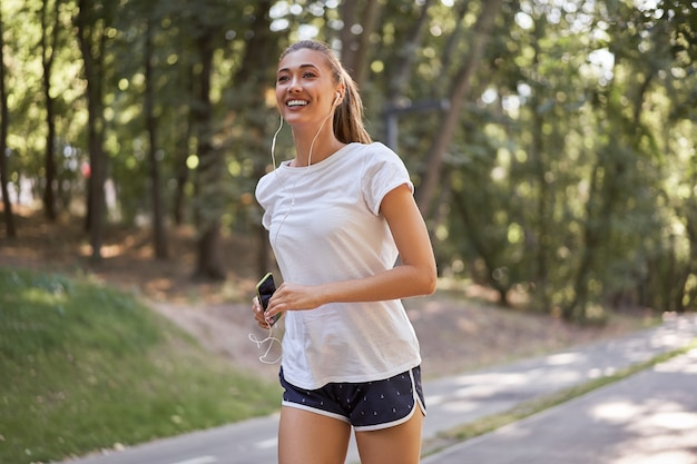 Kobieta zakłada słuchawki do słuchania muzyki przed joggingiem w letnim parku