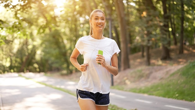 Kobieta zakłada słuchawki do słuchania muzyki przed joggingiem w letnim parku