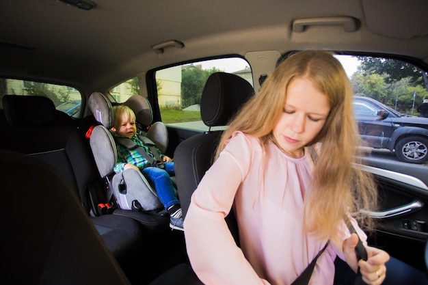 Kobieta zapina pas w samochodzie, gdy zdenerwowany chłopiec siedzi w foteliku samochodowym