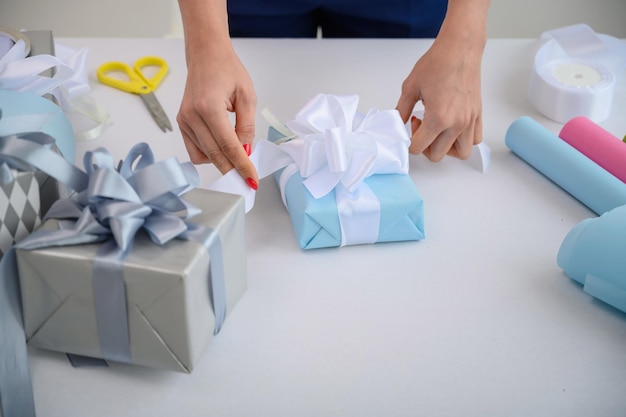 Kobieta zawija pudełka z prezentami na nowy rok Zbliżenie kobiecych dłoni Przygotowuje niespodziankę na dzień matki Papier do pakowania i wstążka na narodziny Projektant zawiązuje kokardkę