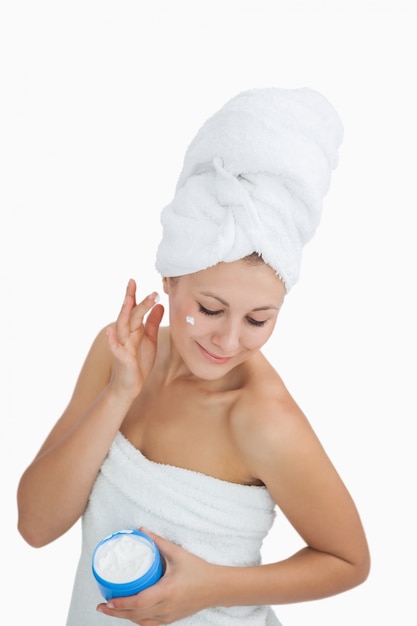 Kobieta zawijająca w ręczniku stosuje śmietankę na twarzy