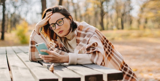 Zdjęcie kobieta zawinięta w koc i za pomocą smartfona