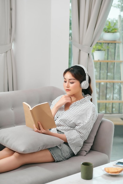 kobieta ze słuchawkami czytając książkę w salonie siedząc na kanapie
