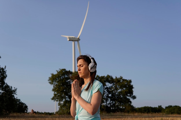 Kobieta Ze Słuchawkami Medytująca Spokojnie Na Zewnątrz O Zachodzie Słońca Z Polem Wiatraków Zrównoważony Rozwój Energii Odnawialnej