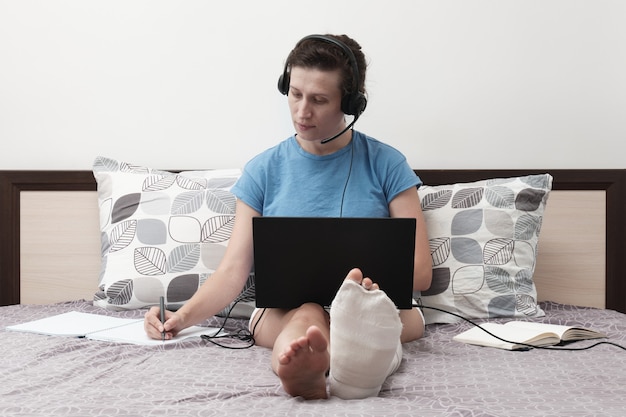 Kobieta ze słuchawkami siedzi na łóżku i trzyma laptopa na kolanach