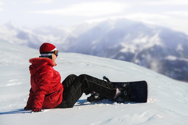 Kobieta ze snowboardem siedząca w śnieżnych górach w tle