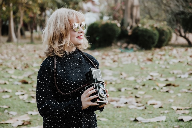 Zdjęcie kobiety fotografii smilling, pozycja i ręka trzyma retro kamerę w plenerowym. rocznika brzmienie