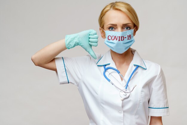 Kobiety lekarka jest ubranym maskę ochronną i lateksowe rękawiczki nad jasnopopielatą ścianą z stetoskopem